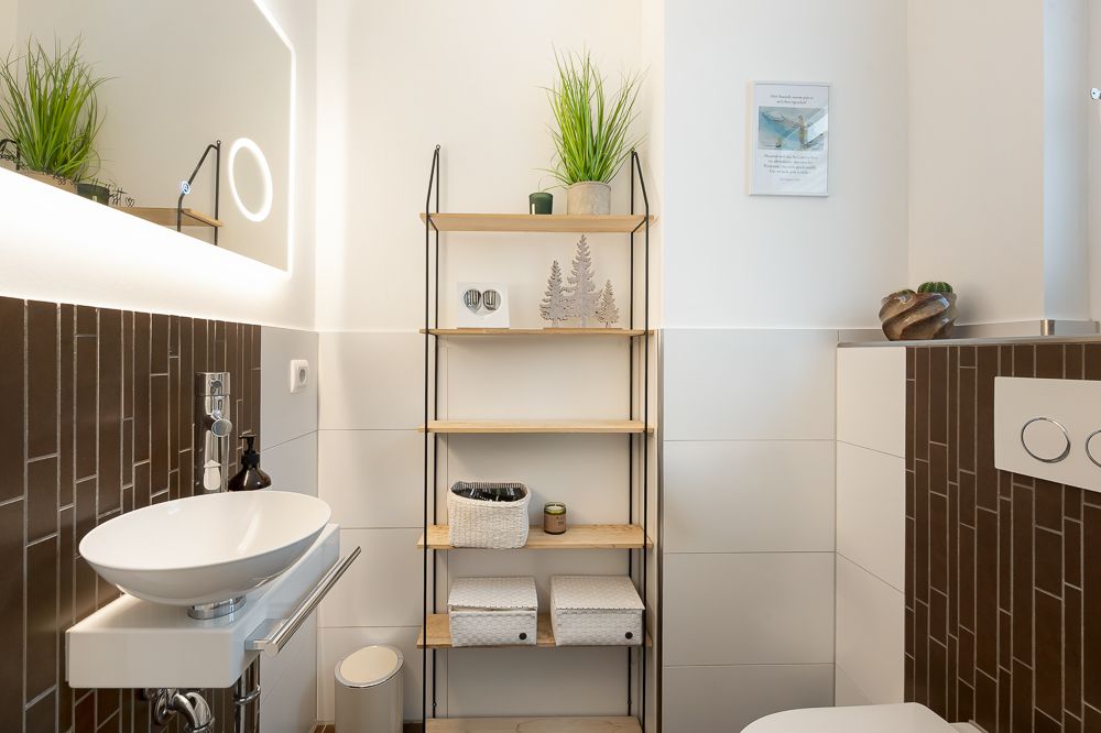 Modernes Badezimmer mit Waschbecken, Regal, Pflanzen und braun-weißen Fliesen.
