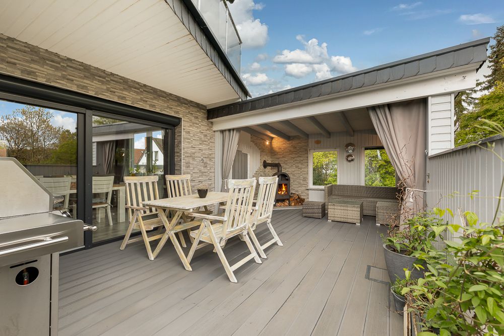 Moderne Terrasse mit Holzboden, Esstisch, Grill und überdachtem Loungebereich mit Ofen.
