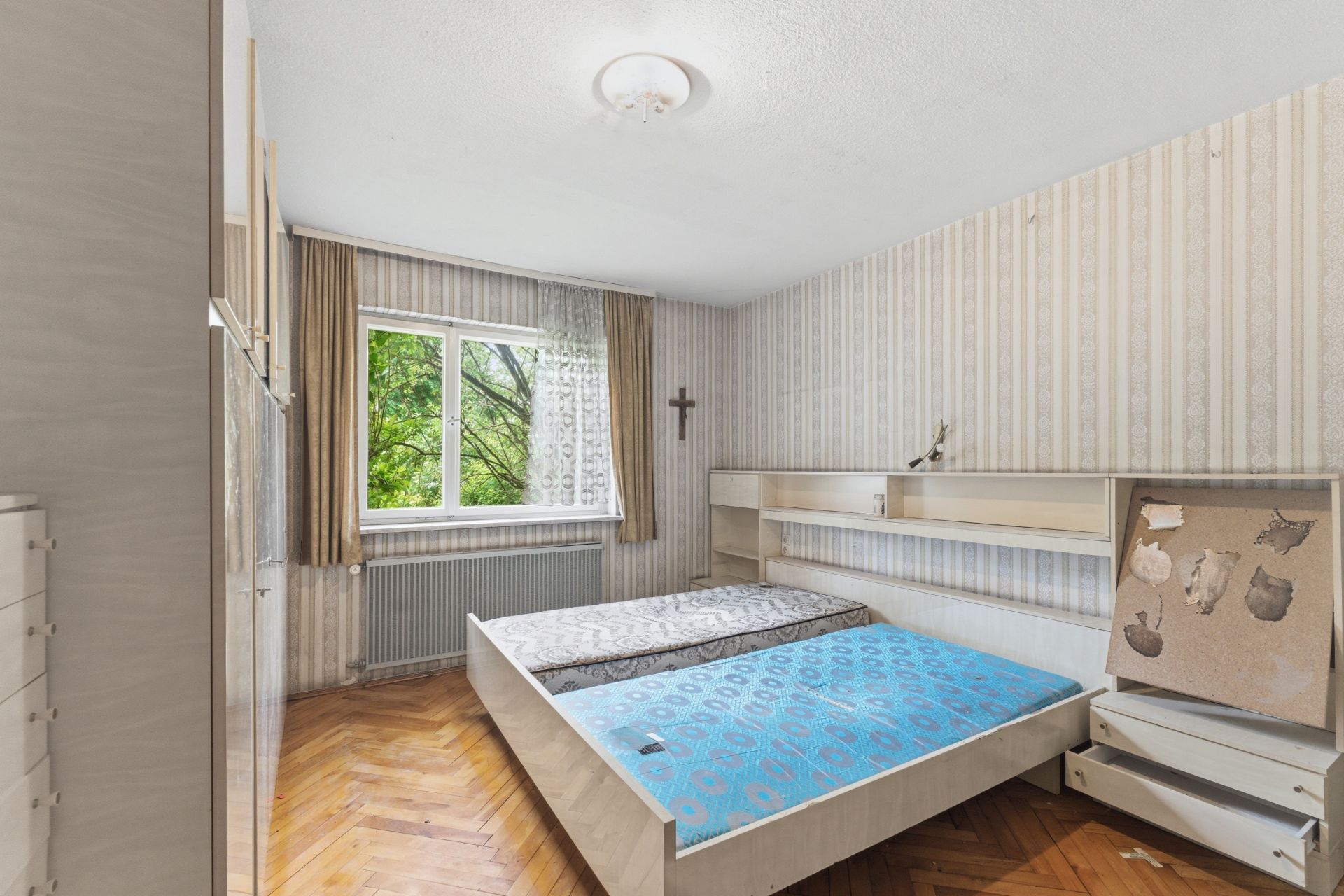 Schlafzimmer mit Doppelbett, Holzfußboden und Fenster mit Blick ins Grüne.