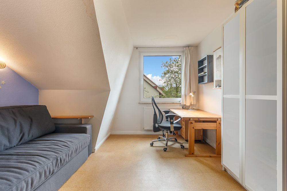 Helles Zimmer mit Sofa, Schreibtisch, Bürostuhl, Fenster und Kleiderschrank.