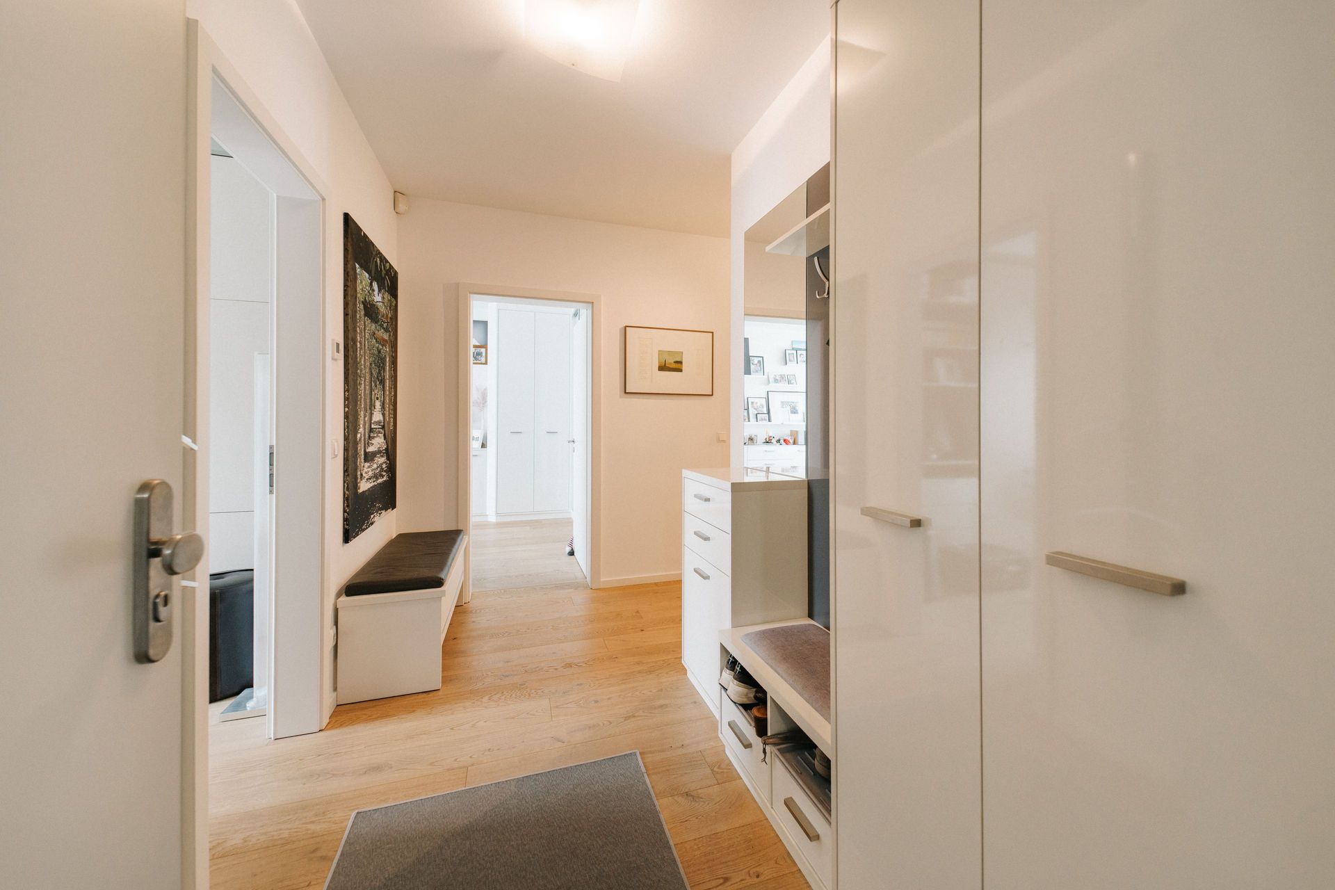 Heller Flur mit Holzboden, weißen Schränken und einer Sitzbank an der Wand.