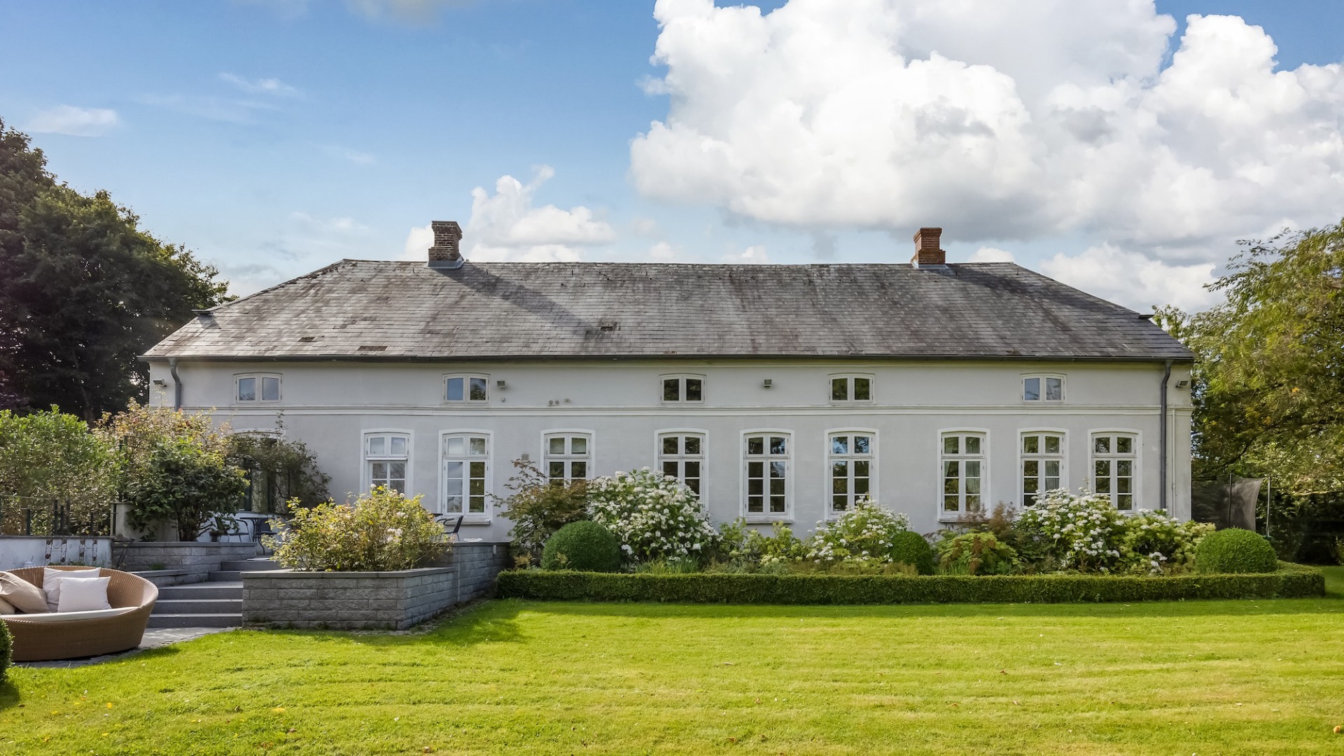 Großes, weißes Haus mit vielen Fenstern und gepflegtem Garten im Vordergrund.