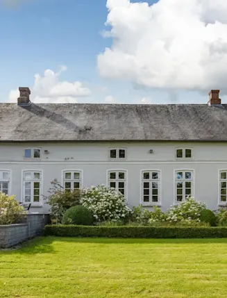Großes, weißes Haus mit vielen Fenstern und gepflegtem Garten im Vordergrund.