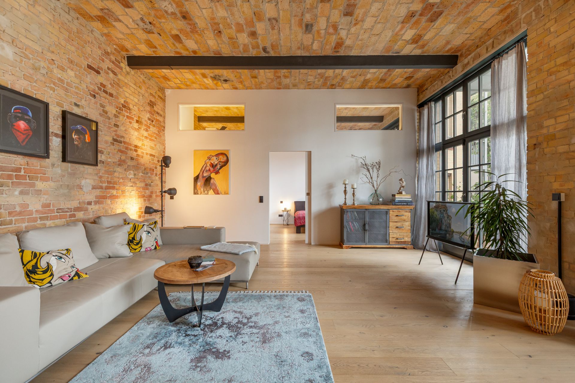 Modernes Wohnzimmer mit Backsteinwänden, großem Fenster, Sofa, Couchtisch, Teppich und Bildern an der Wand.