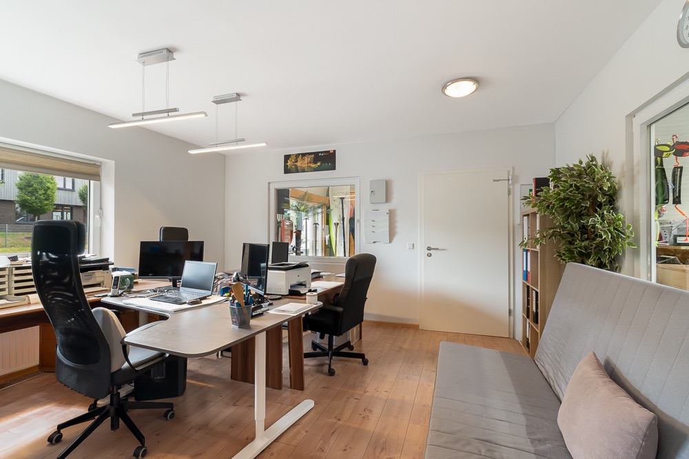 Helles Arbeitszimmer mit zwei Schreibtischen, Regalen, Sofa und großem Fenster mit Blick nach draußen.