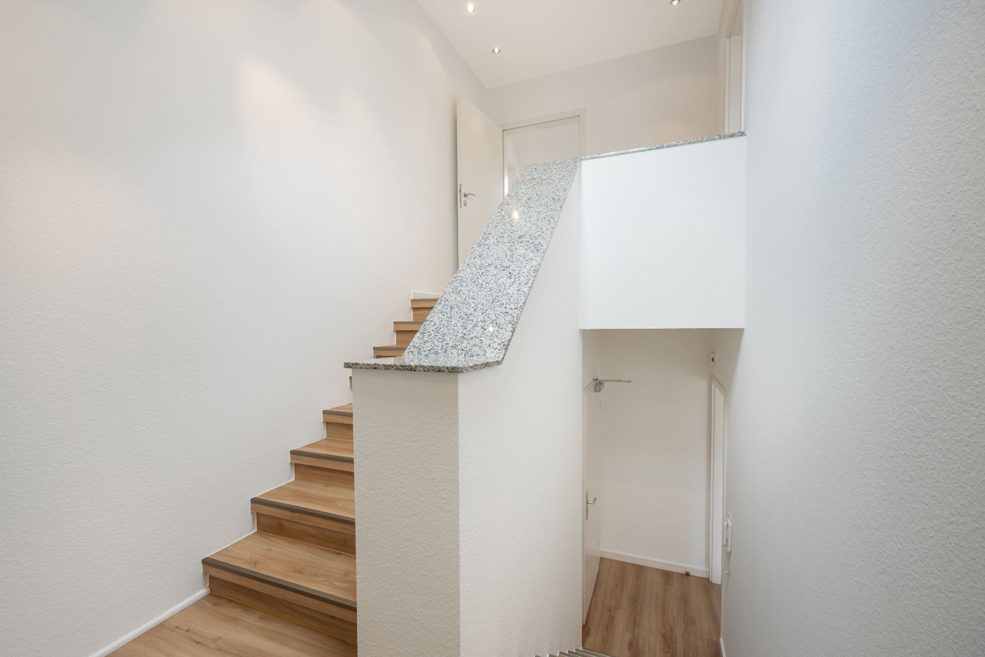 Heller Treppenaufgang mit Holzstufen und weißem Geländer in einem Wohnhaus.