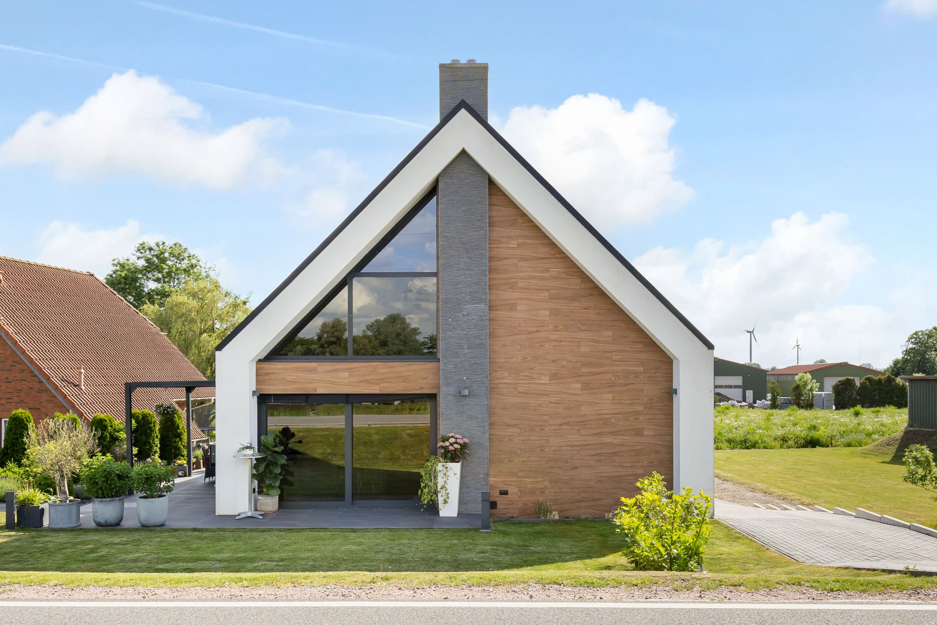 Modernes Einfamilienhaus mit Satteldach, Holzfassade und großen Fenstern, davor einige Pflanzen.