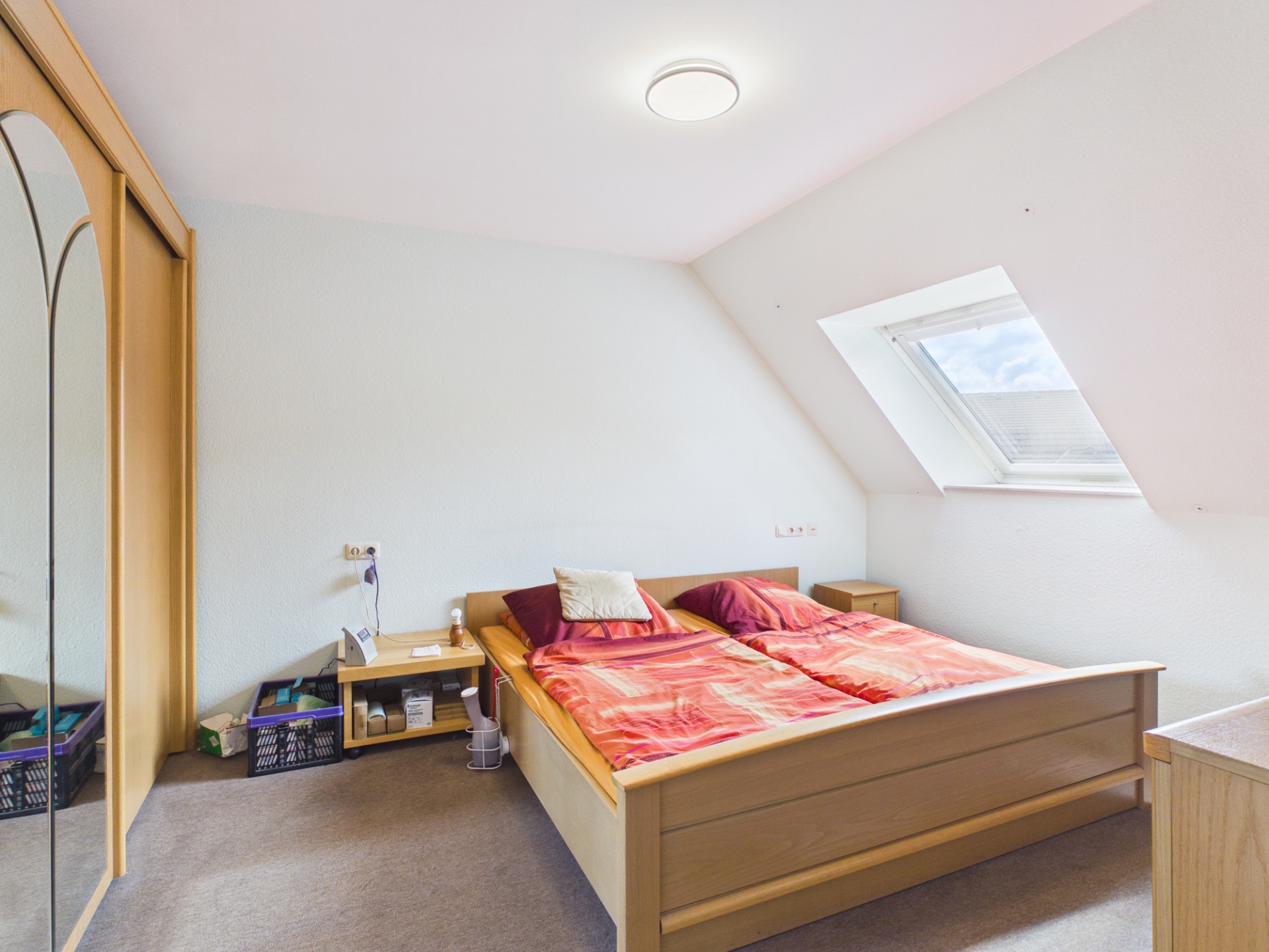 Schlafzimmer mit Dachfenster, Doppelbett, Nachttischen und Spiegelschrank.