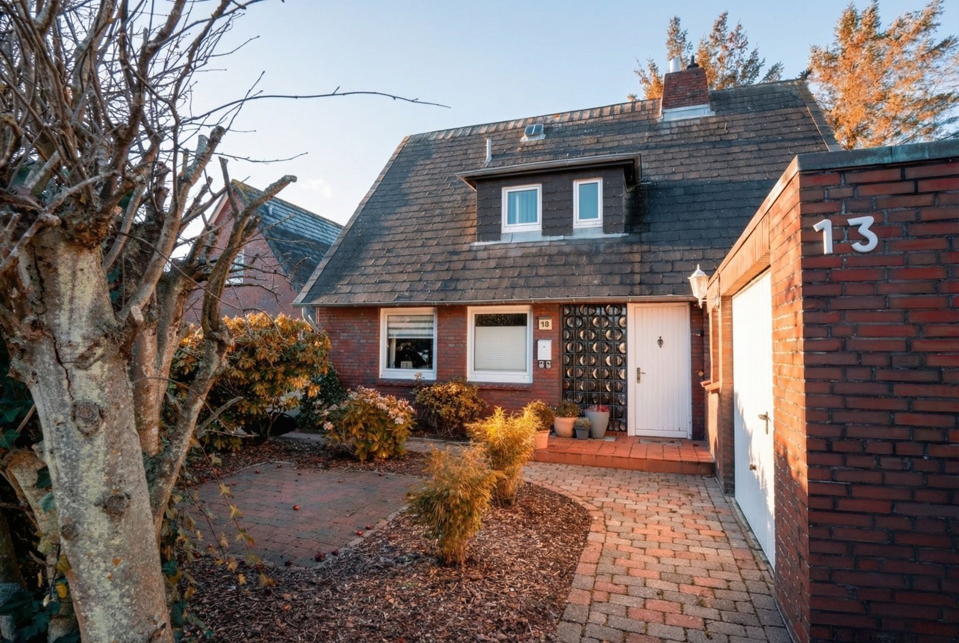Einfamilienhaus mit dunklem Dach, Vorgarten, gepflastertem Weg und Garage mit der Hausnummer 13.