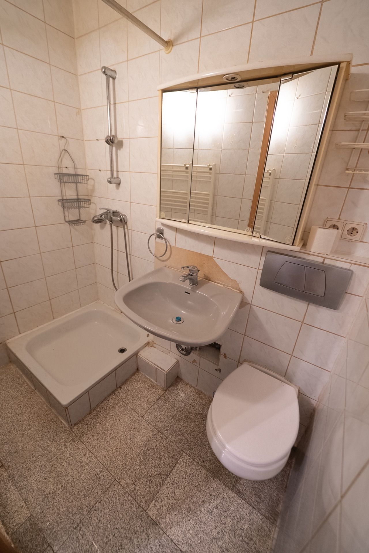Kleines Badezimmer mit Dusche, Waschbecken, Spiegel und Toilette.