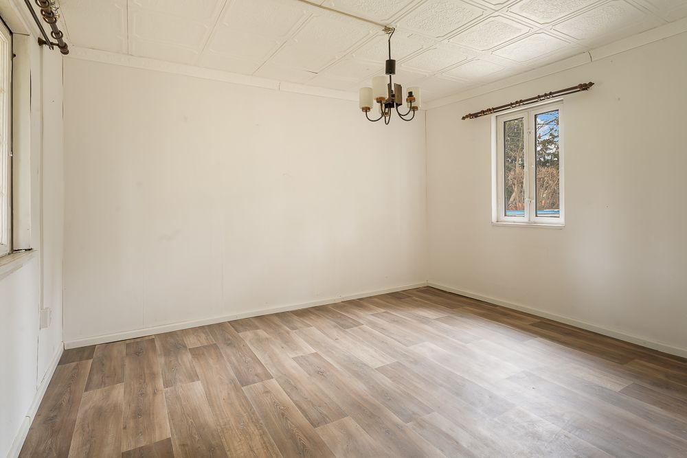 Leerer Raum mit holzfarbenem Boden, zwei Fenstern und einer Deckenlampe.