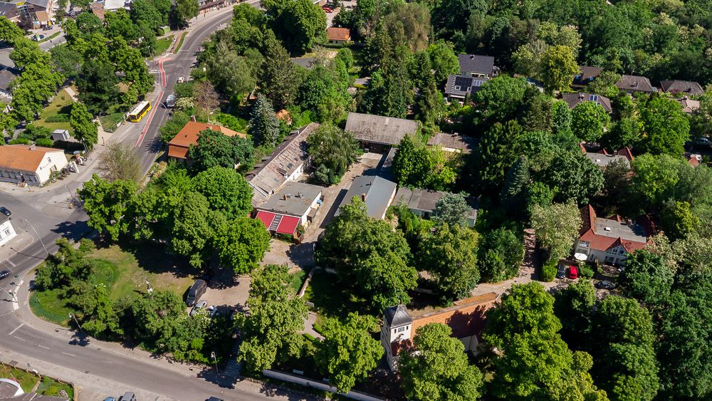 Luftaufnahme von Wohnhäusern und Straßen in einer grünen, baumreichen Umgebung.