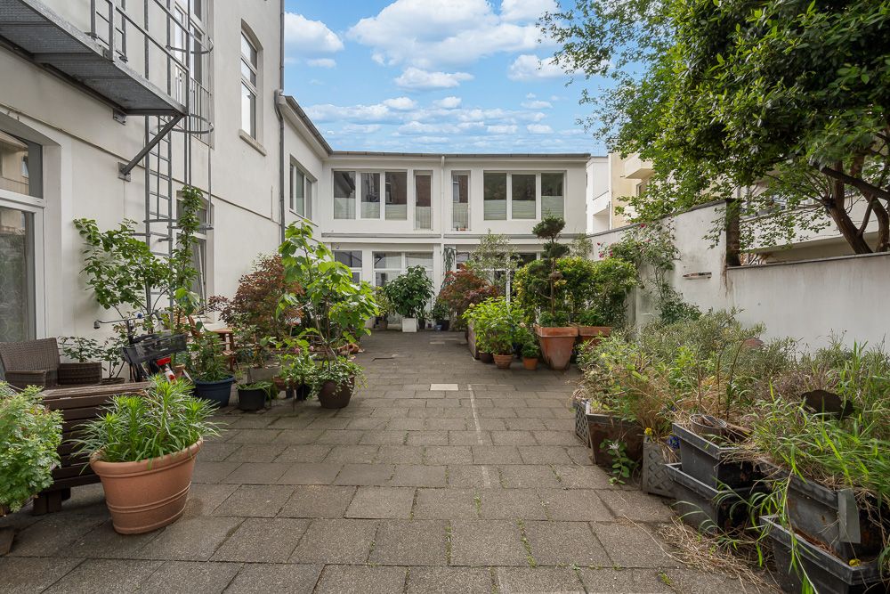 Gepflasterter Innenhof mit vielen Topfpflanzen und weißem Wohngebäude im Hintergrund.