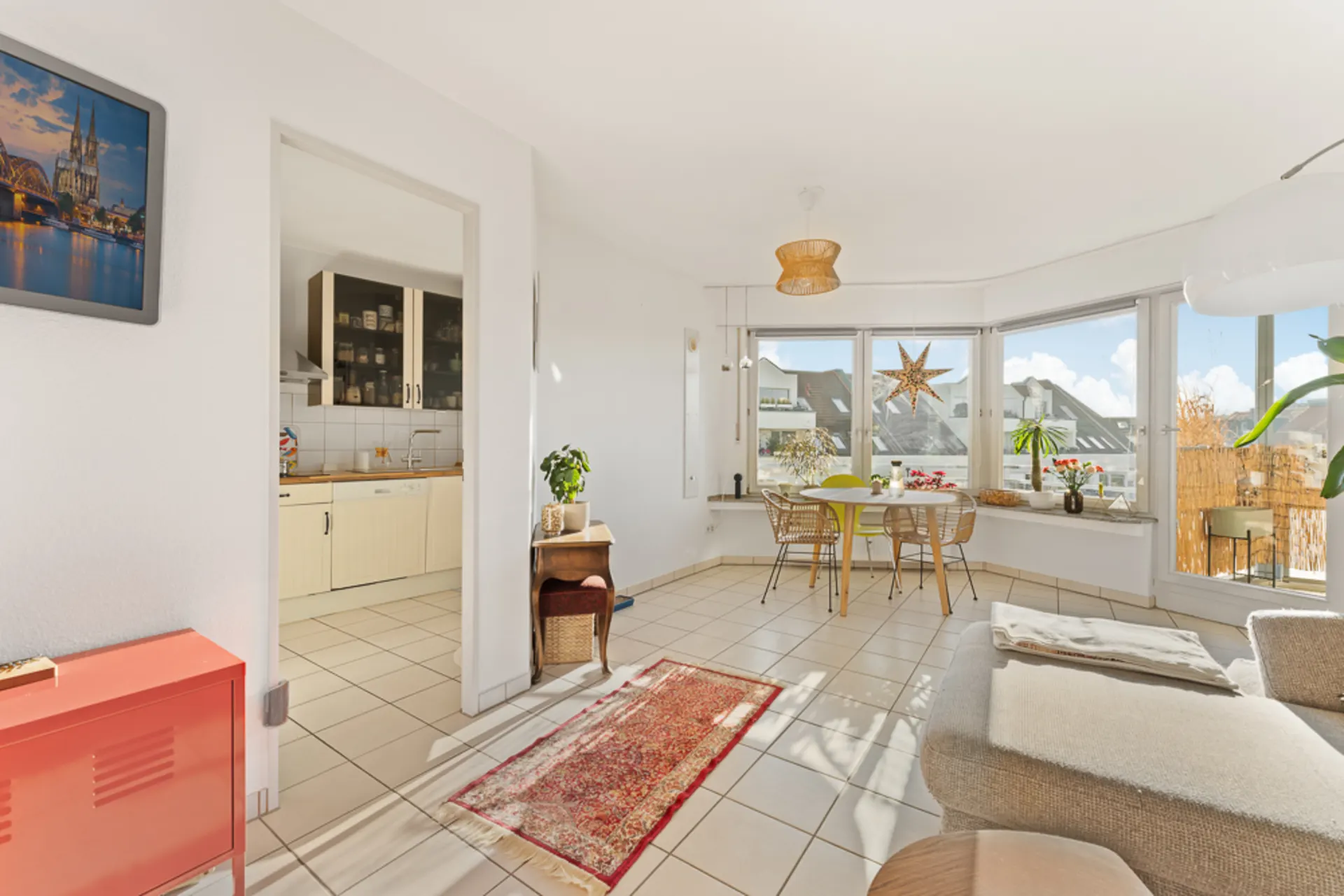 Helles Wohnzimmer mit Essbereich, großen Fenstern, Zugang zur Küche und Balkon.