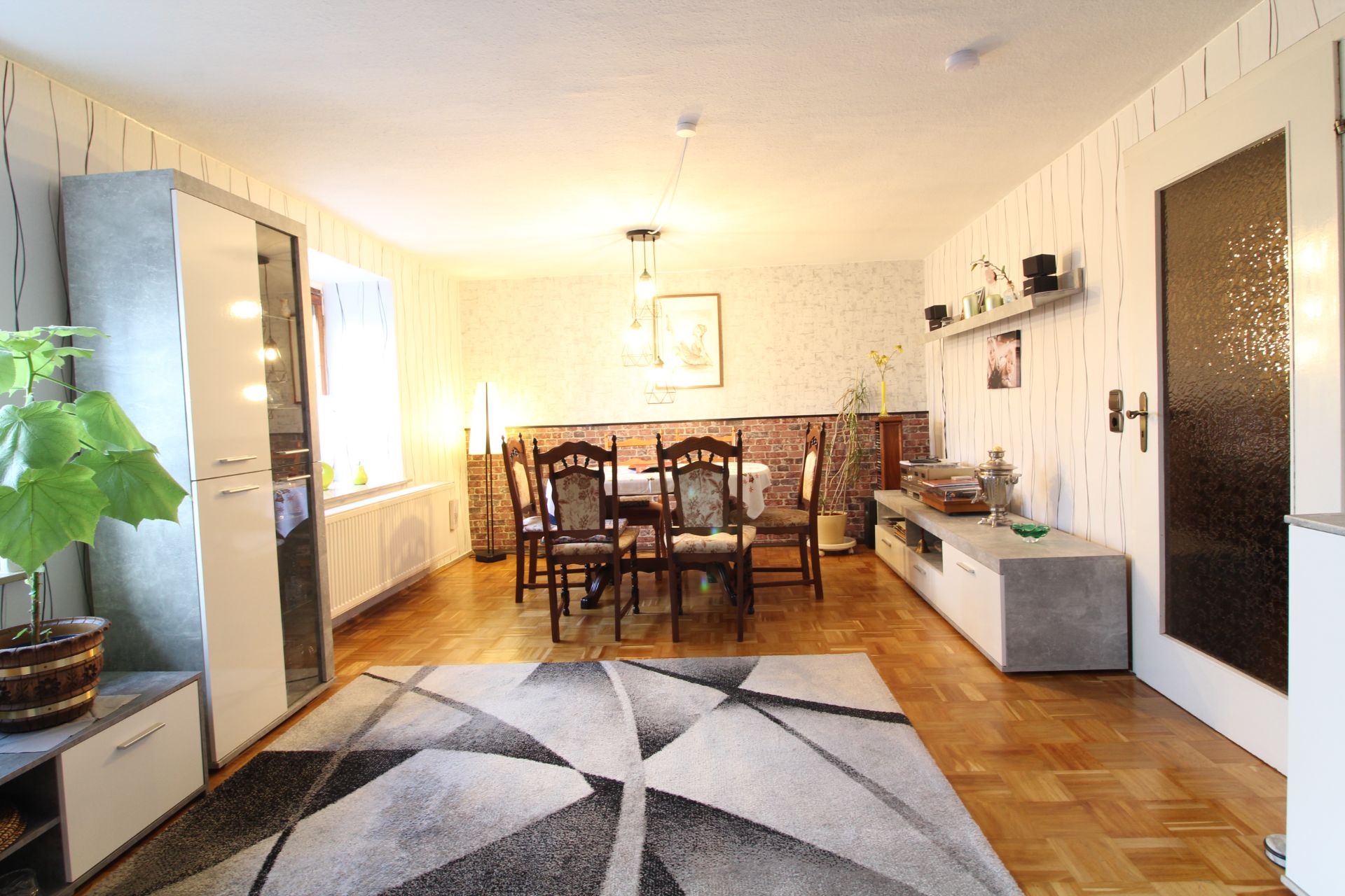 Helles Wohnzimmer mit Esstisch, Stühlen, Teppich und Schrankmöbeln auf Parkettboden.