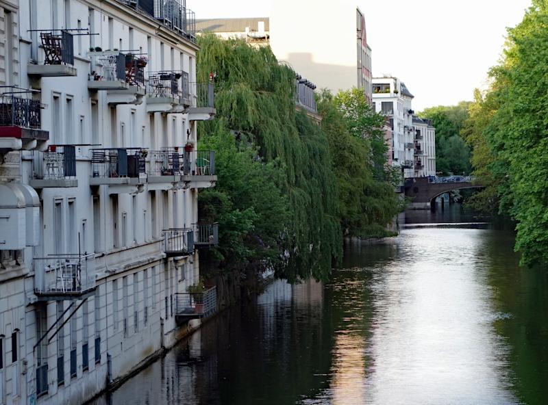 Wohnhäuser mit Balkonen an einem Fluss, umgeben von vielen grünen Bäumen.