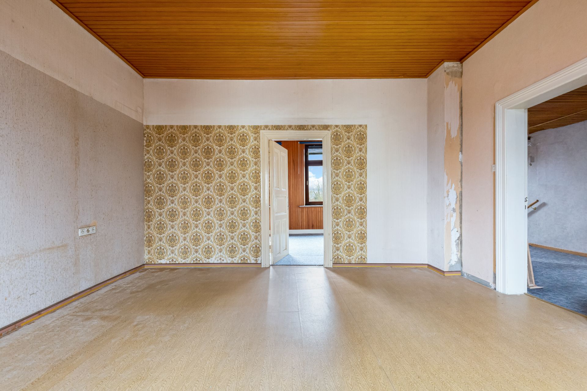 Leerer Raum mit gemusterten Tapeten, Holzboden und Holzdecke, offene Türen zu weiteren Räumen.