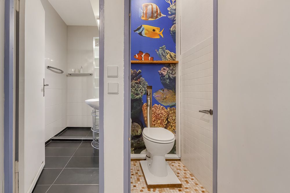 Toilette mit bunter Unterwasser-Wanddekoration und Fliesenboden.