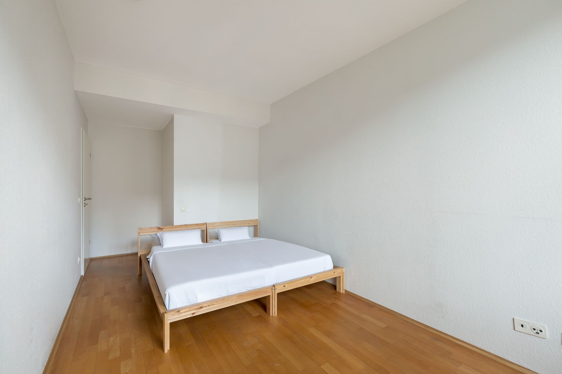 Schlafzimmer mit Holzboden, einem einfachen Doppelbett und weißen Wänden.