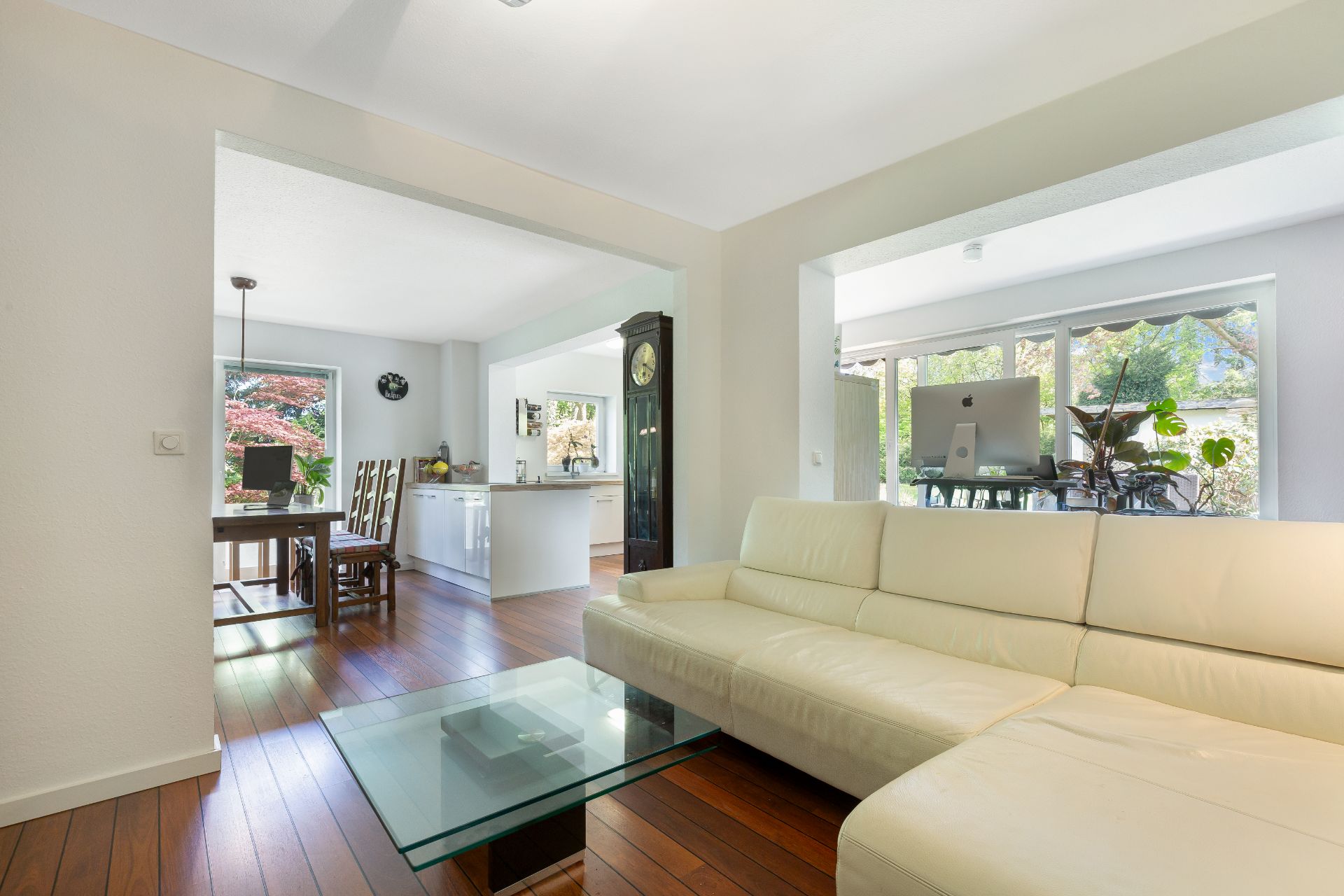 Helles Wohnzimmer mit beiger Eckcouch, Glastisch und Blick in Esszimmer und Küche.