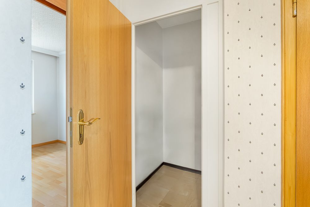 Offene Holztür mit Blick in einen kleinen, leeren Raum mit hellen Wänden.