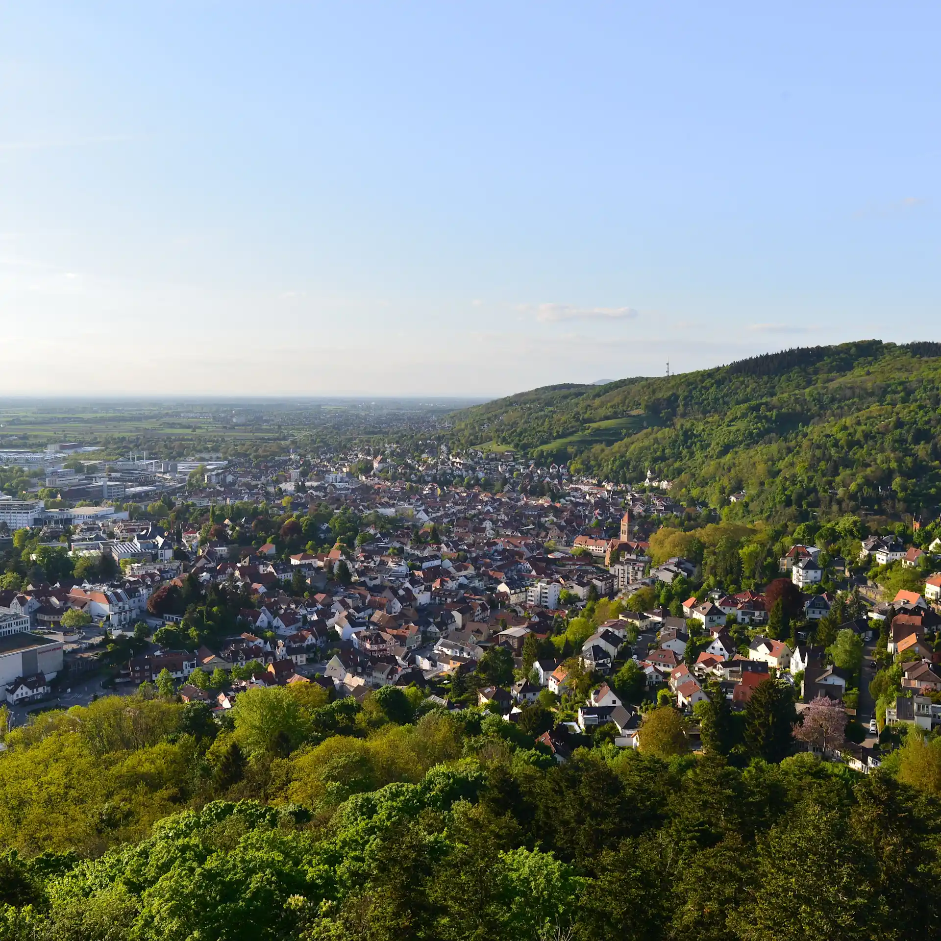 Blick auf eine Stadt mit vielen Häusern und umliegenden grünen Hügeln bei klarem Himmel.