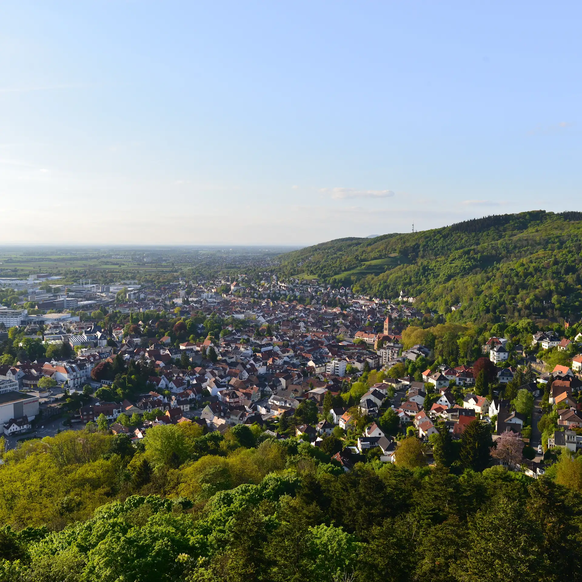 Blick auf eine Stadt mit vielen Häusern und umliegenden grünen Hügeln bei klarem Himmel.