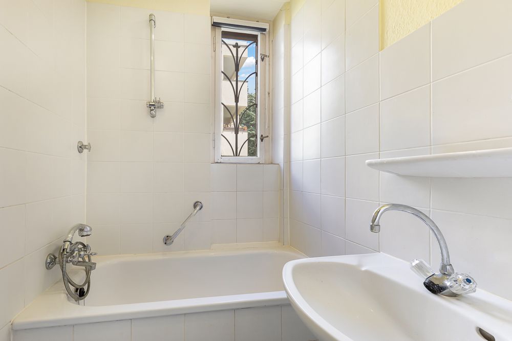 Badezimmer mit Badewanne, Waschbecken und kleinem Fenster mit Gitter.