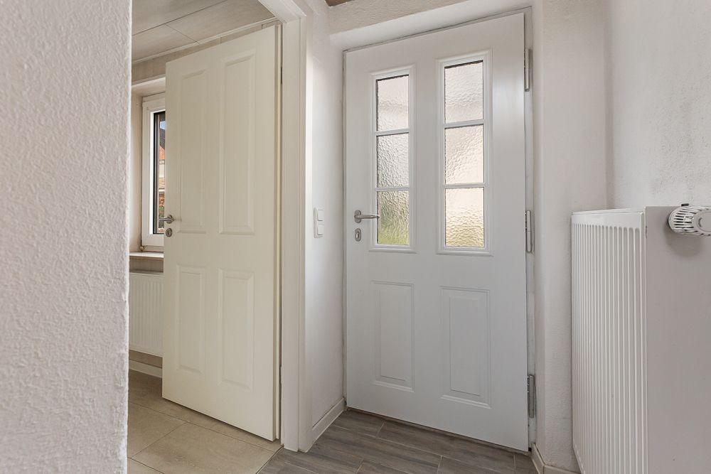 Heller Flur mit weißer Tür, offenem Fenster und Heizkörper.