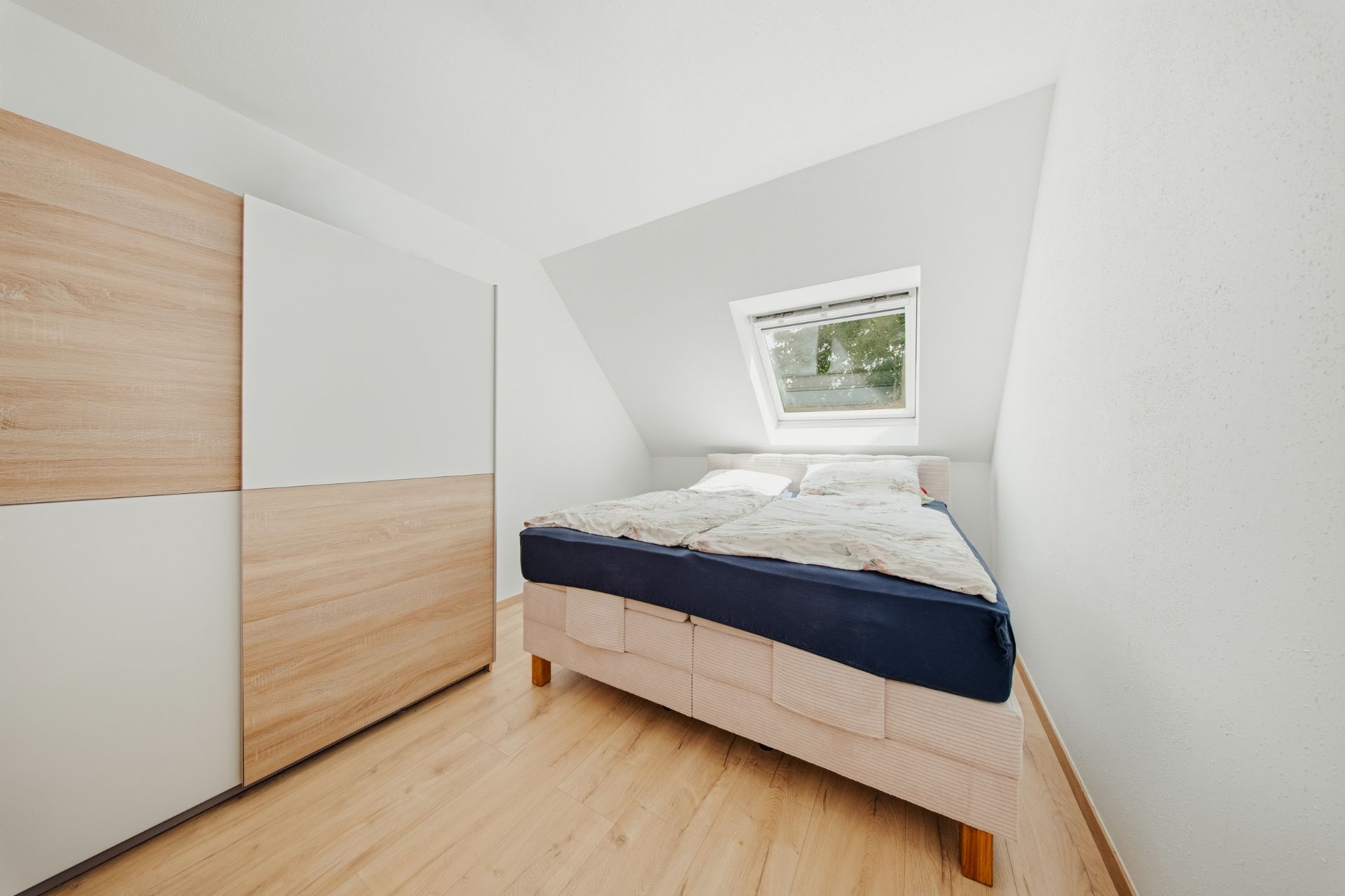 Helles Schlafzimmer mit Doppelbett, Kleiderschrank und Dachfenster.