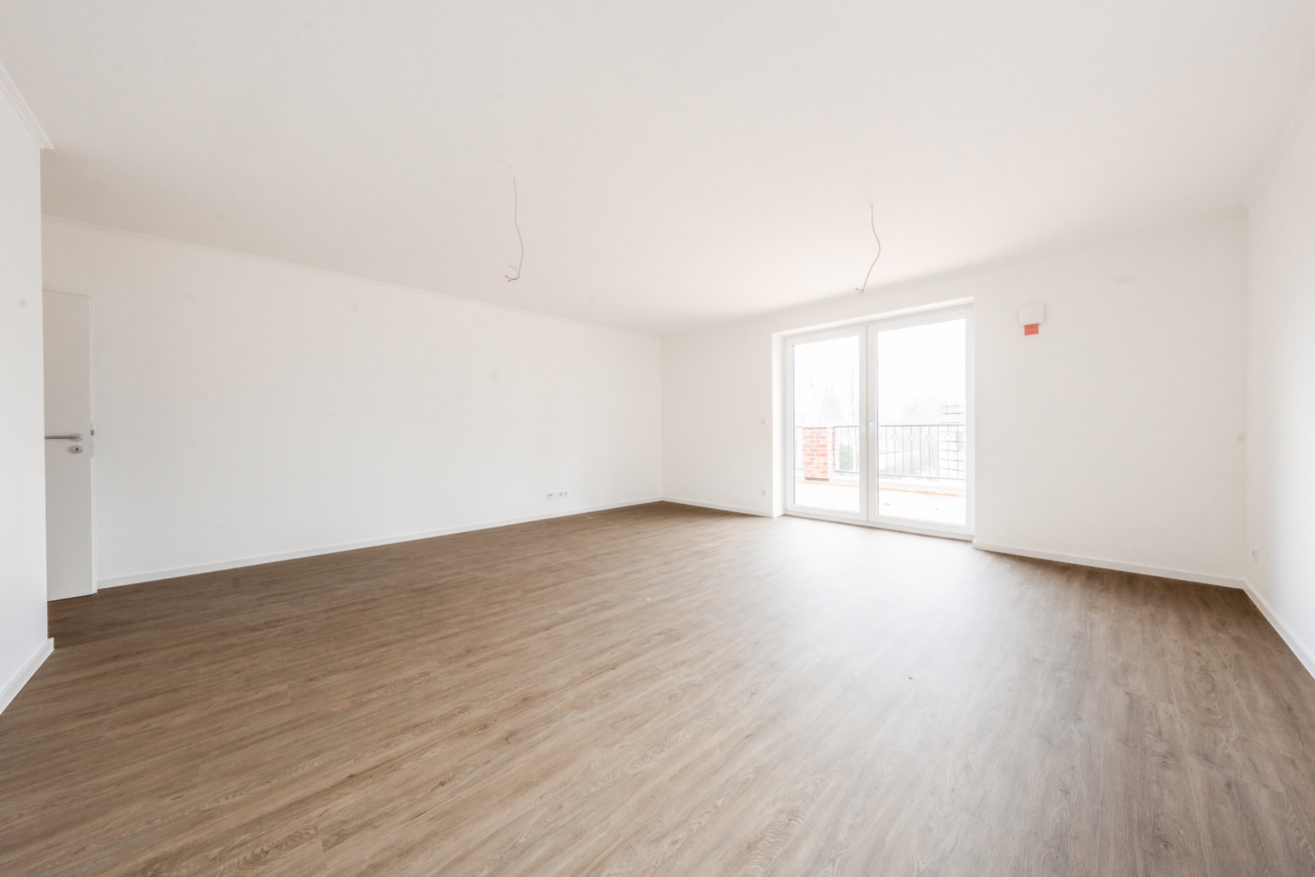 Leerer, heller Raum mit Holzboden und großen Fenstertüren zur Terrasse.