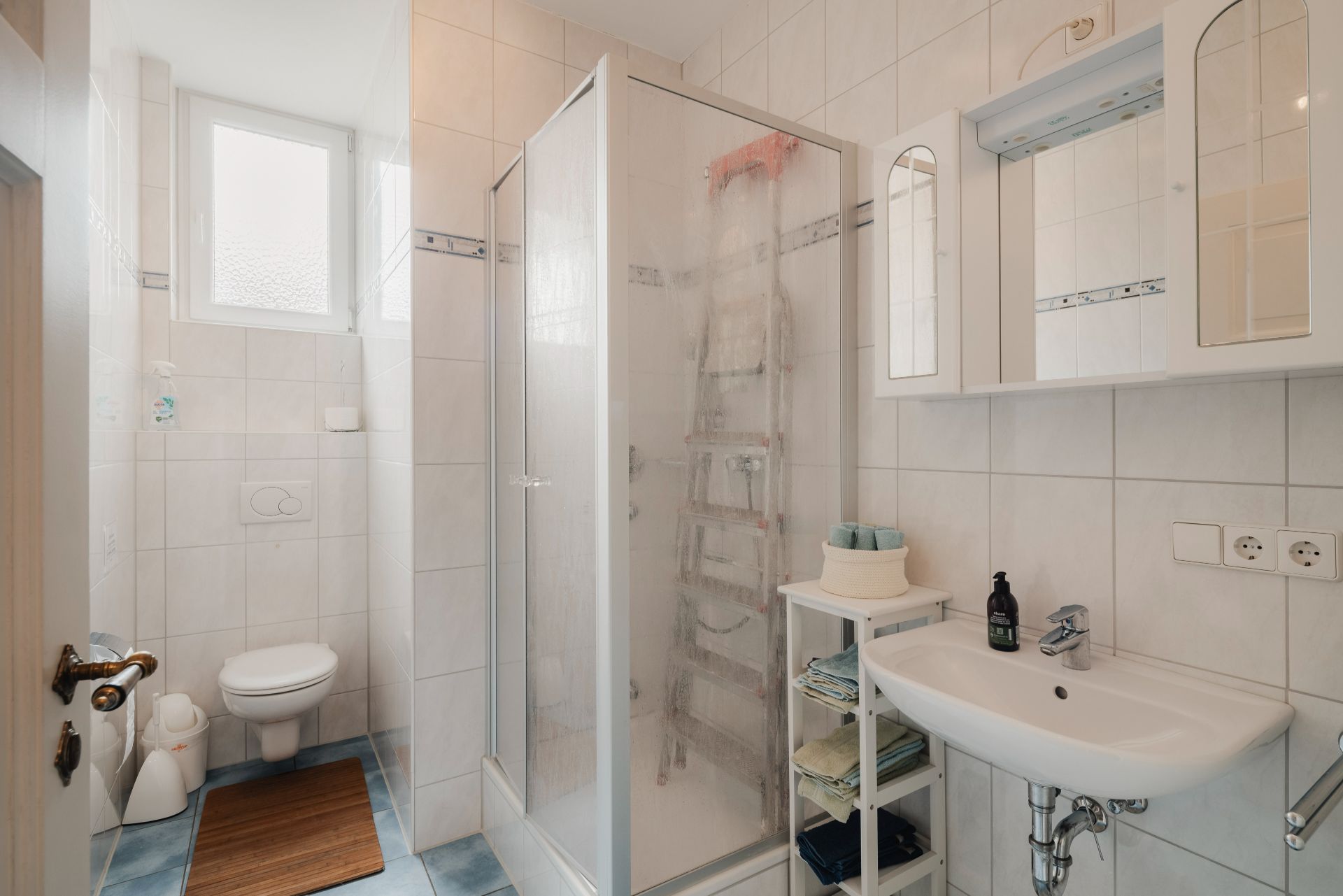 Helles Badezimmer mit Dusche, WC, Waschbecken und Spiegelschrank.