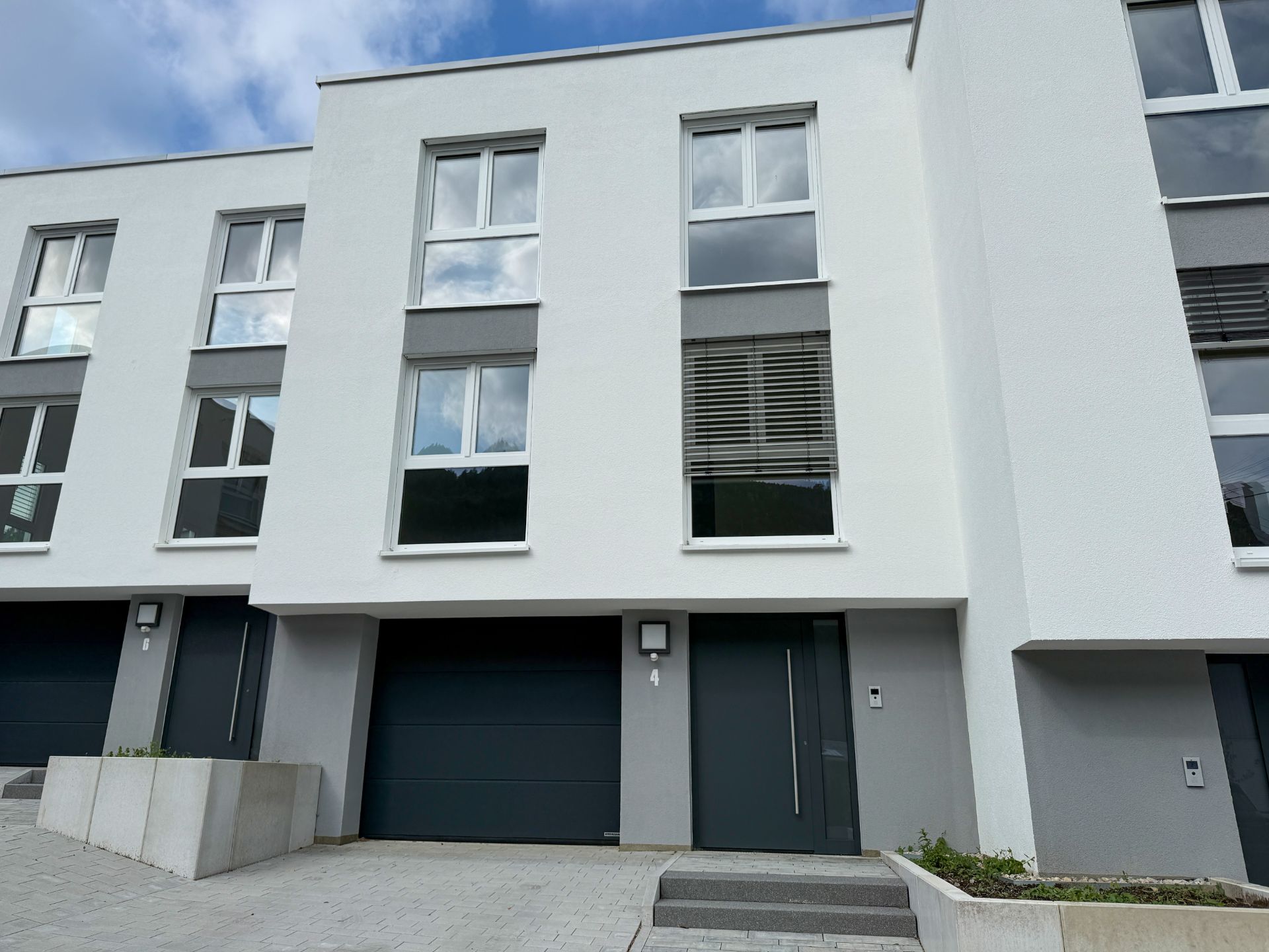 Moderne weiße Reihenhausfassade mit großer Garage und Eingangstür, davor gepflasterter Weg.