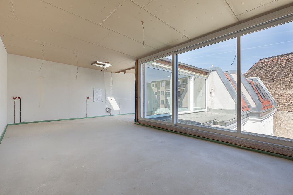 Leerer, heller Raum mit großen Fenstern und Blick auf Nachbargebäude, unfertiger Boden.