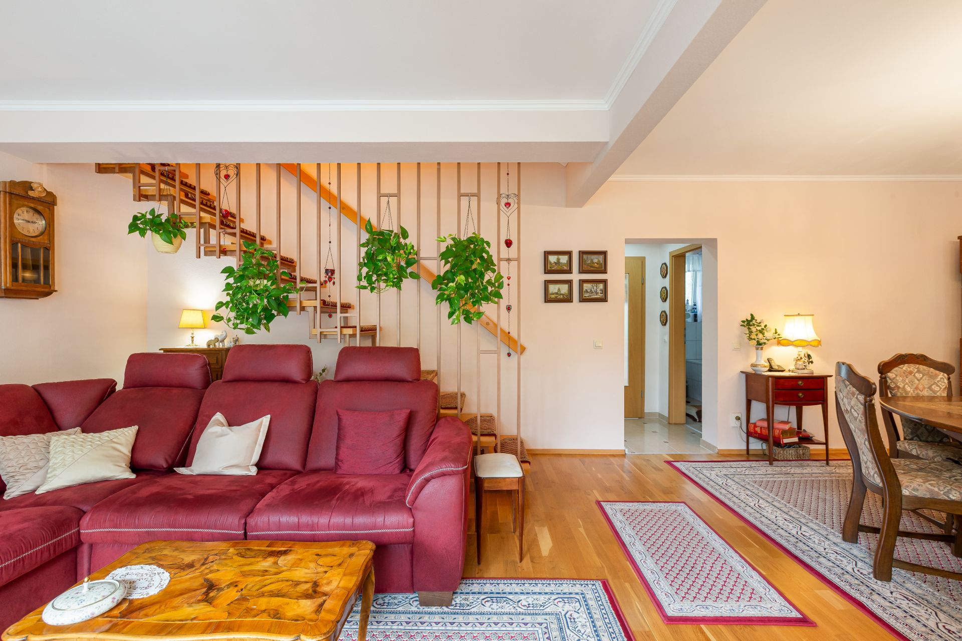 Wohnzimmer mit rotem Sofa, Holztisch, Treppe und mehreren Zimmerpflanzen an der Wand.