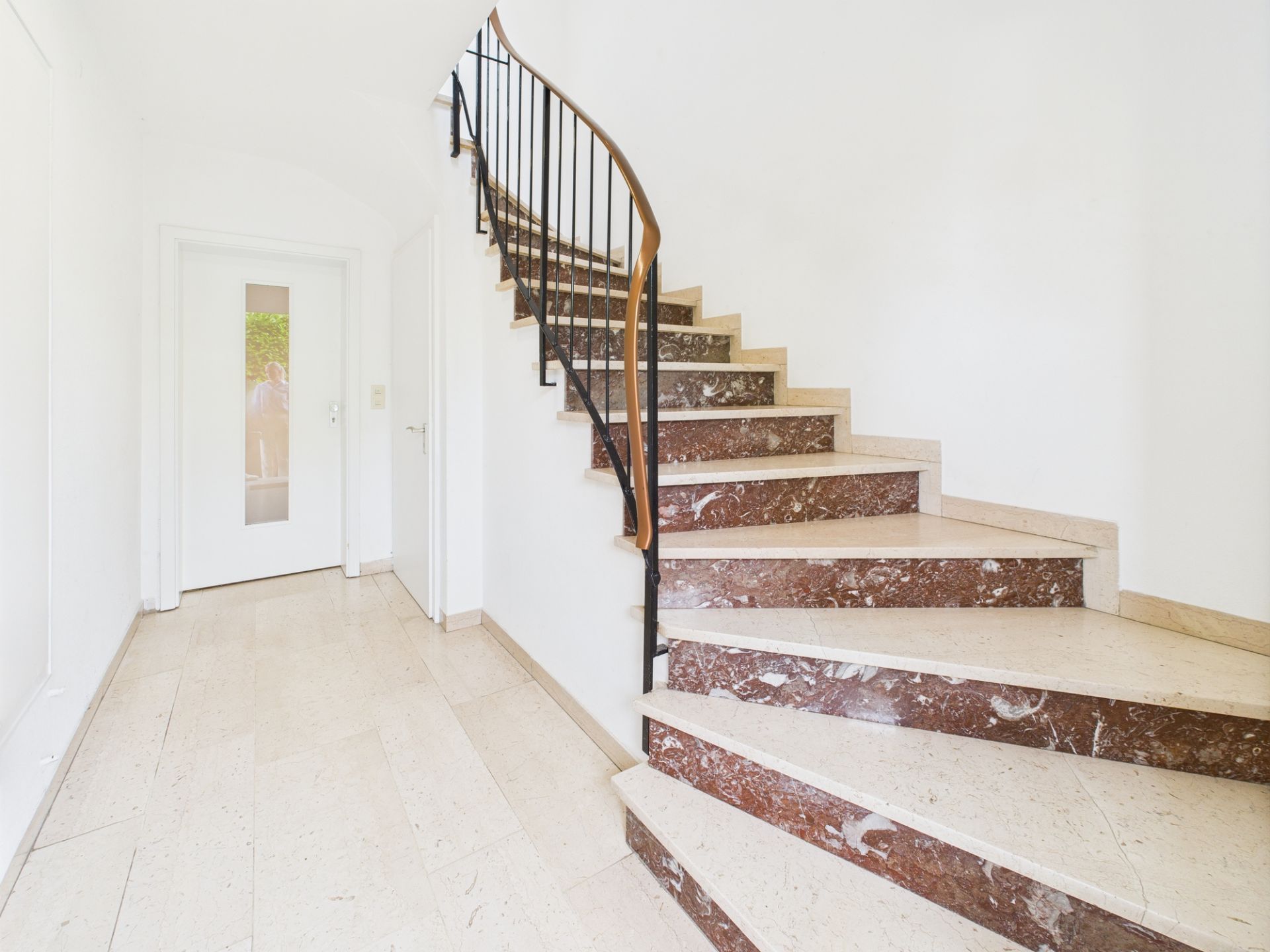 Heller Flur mit einer Treppe aus Marmor und einem weißen Türrahmen.