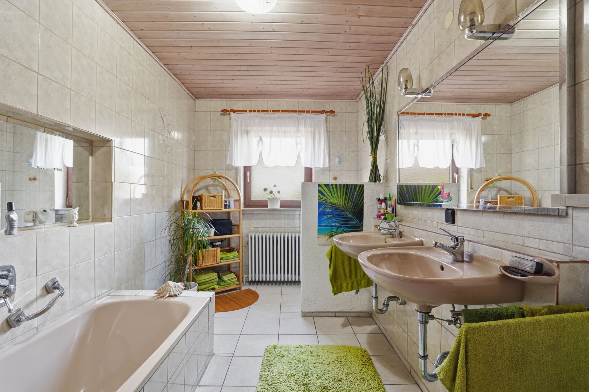 Helles Badezimmer mit Badewanne, zwei Waschbecken, großem Spiegel und grünen Handtüchern.