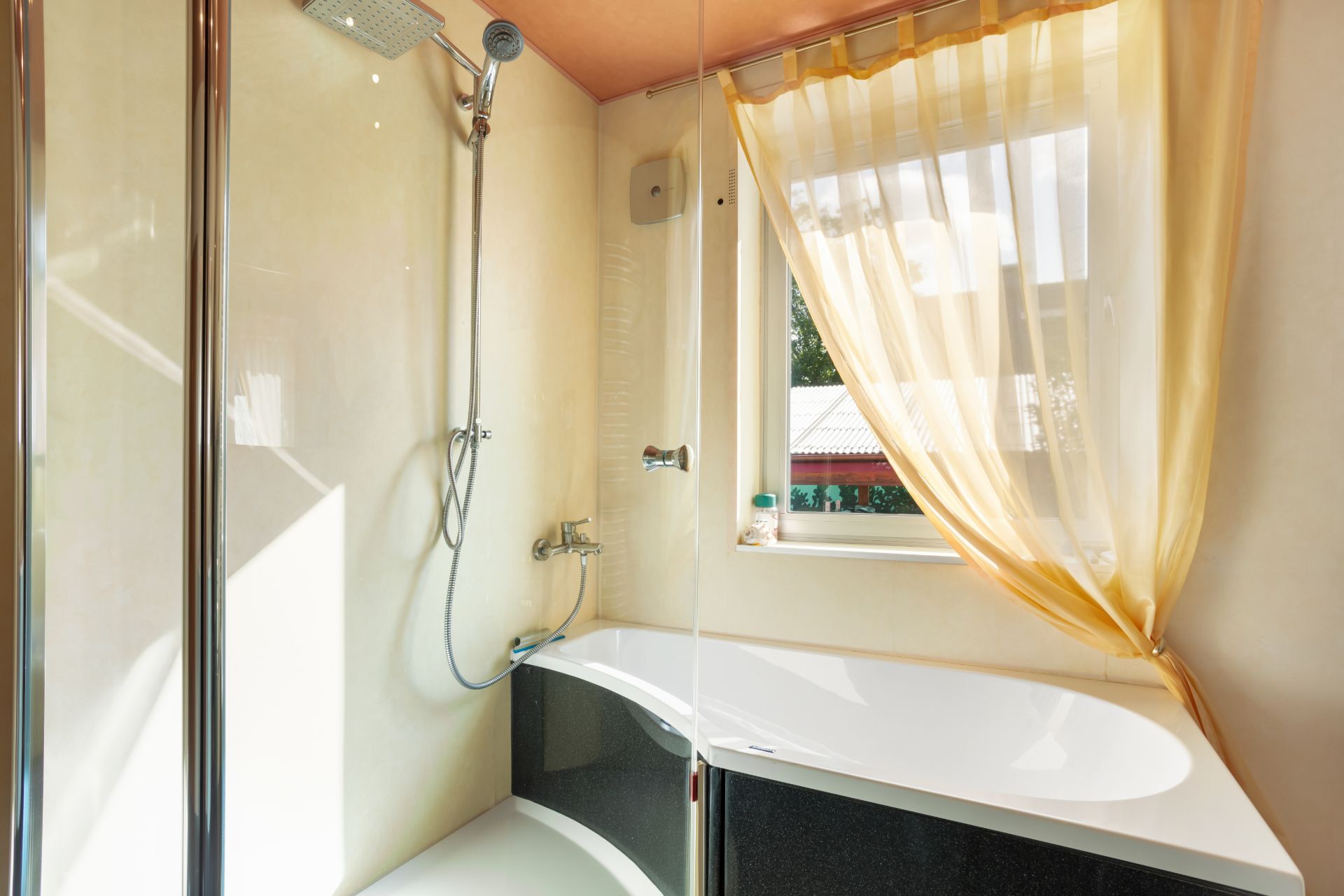 Badezimmer mit Badewanne, Dusche und Fenster mit gelbem Vorhang.
