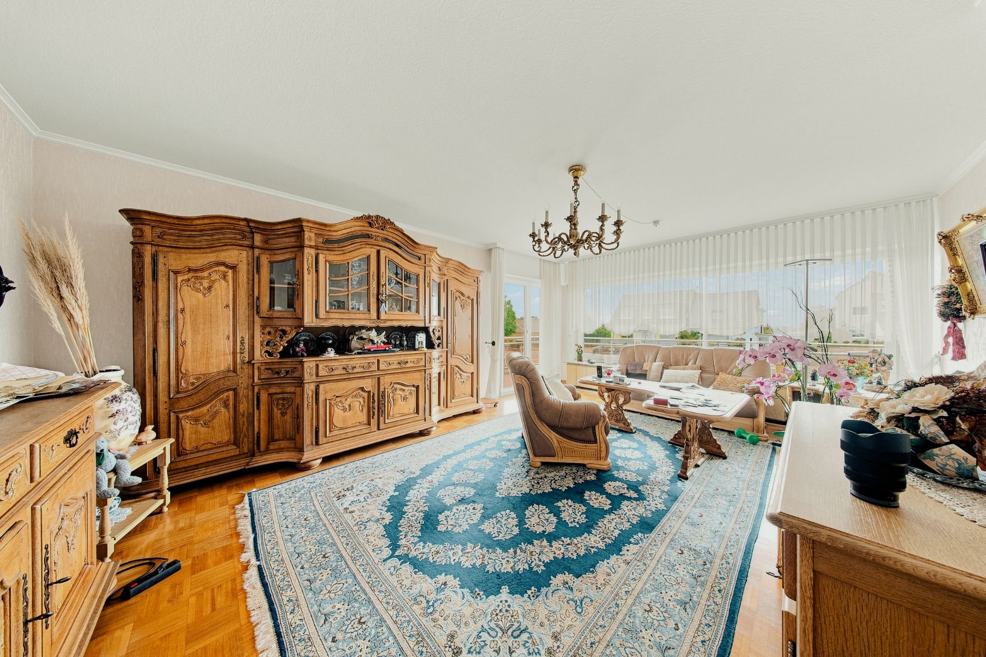 Helles Wohnzimmer mit Holzmöbeln, Teppich, Sessel, Sofa, Couchtisch und großem Fenster.