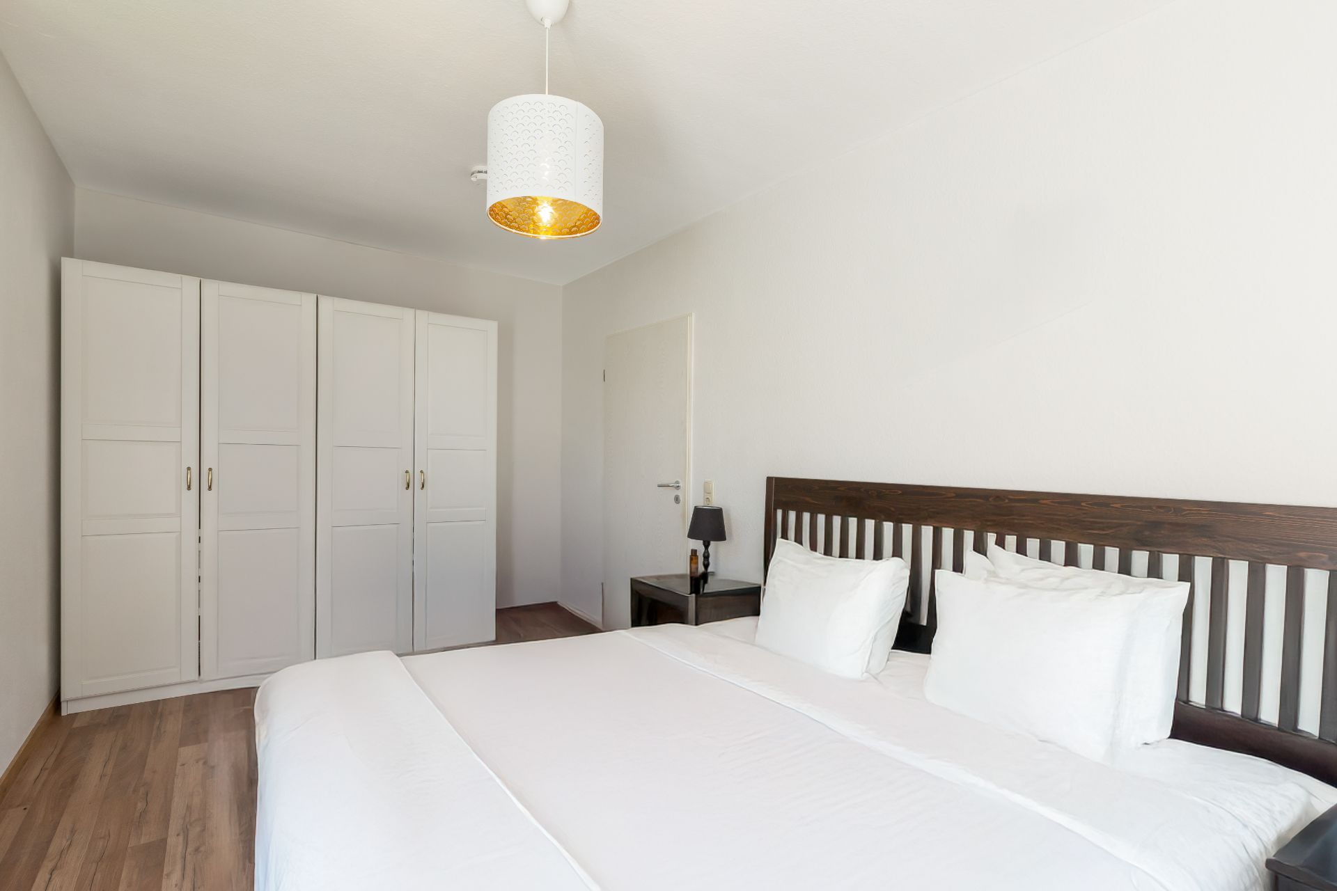 Helles Schlafzimmer mit Doppelbett, weißen Schränken und Nachttisch mit Lampe.