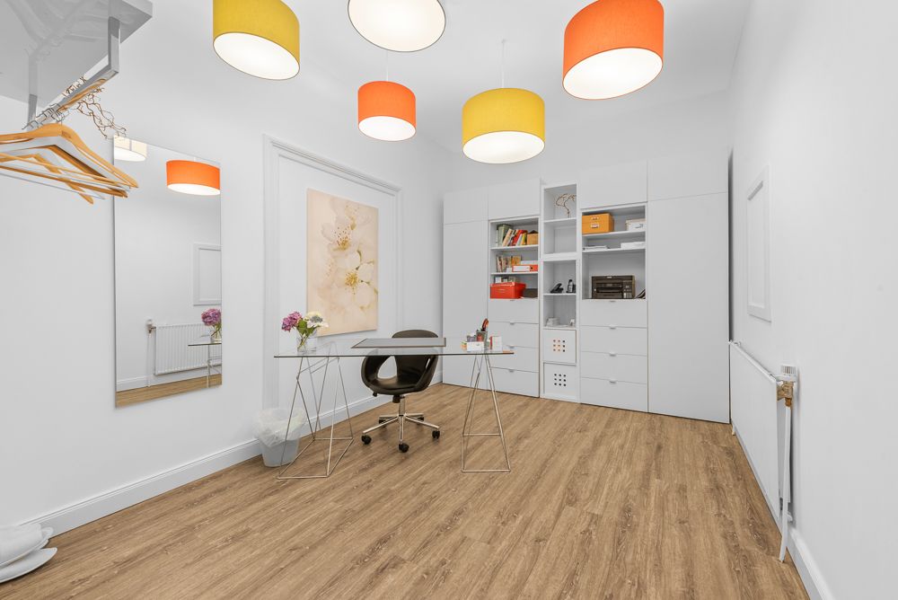Helles Arbeitszimmer mit Glas-Schreibtisch, Bücherregal, Spiegel und bunten Deckenlampen.
