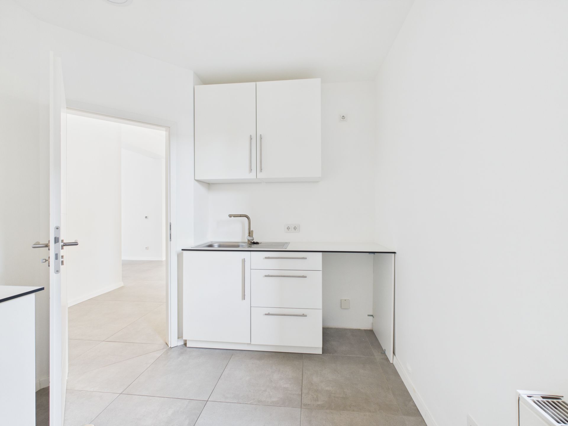 Helle, kleine Einbauküche mit weißen Schränken, Spüle und offenem Unterschrank.