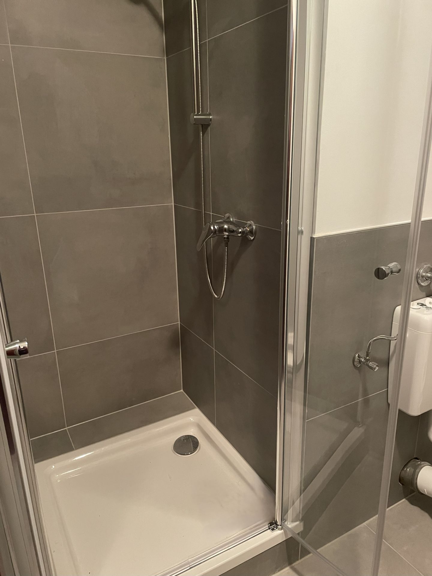 Moderne Dusche mit grauen Fliesen und verstellbarer Duschbrause in einem Badezimmer.
