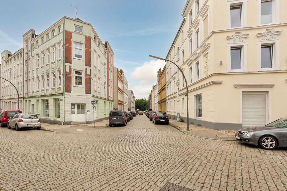 Gepflasterte Straße mit geparkten Autos und mehrstöckigen Wohnhäusern an einer Straßenecke.