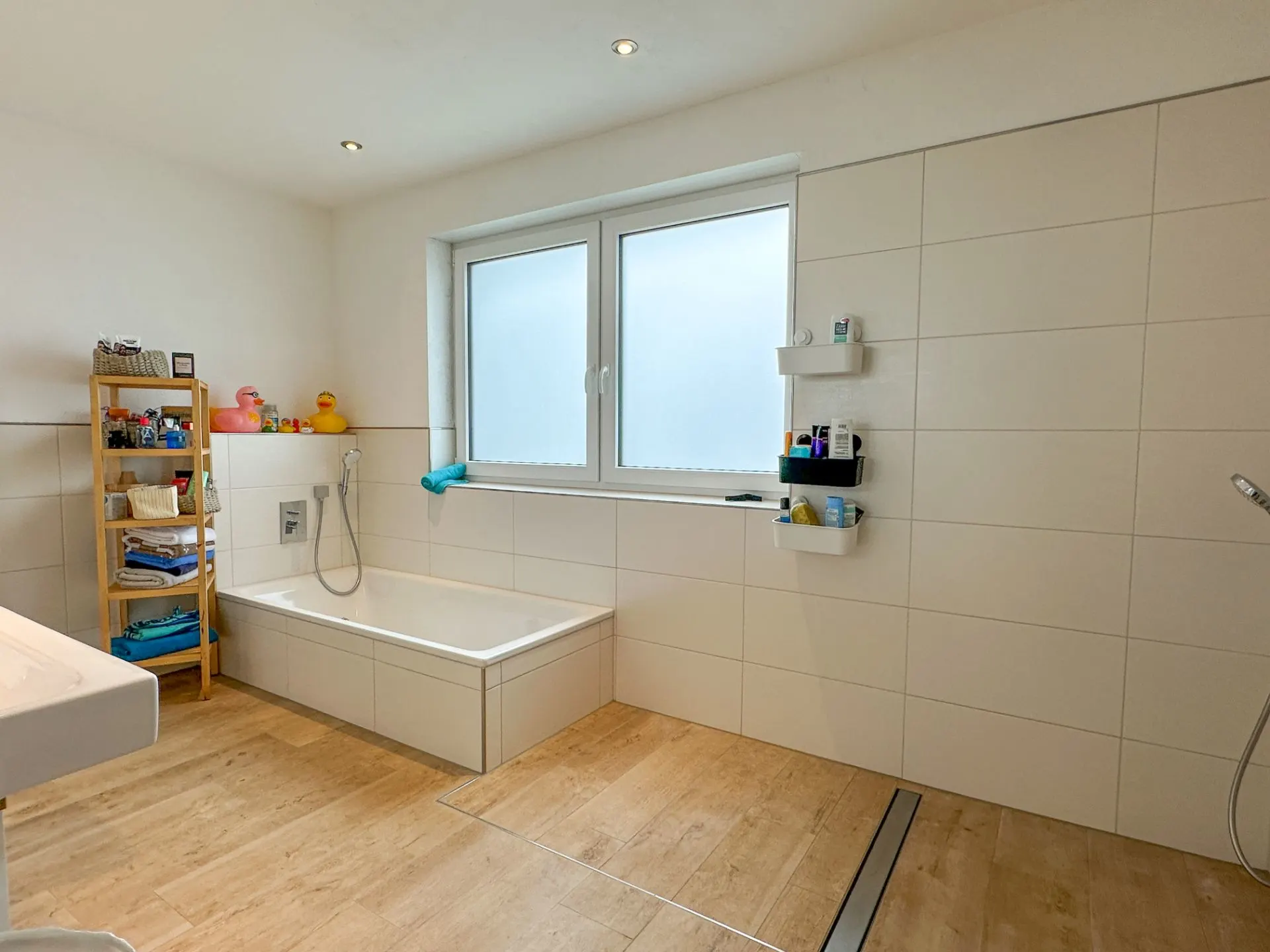 Modernes Badezimmer mit Badewanne, Regalen und großem Fenster mit Milchglas.