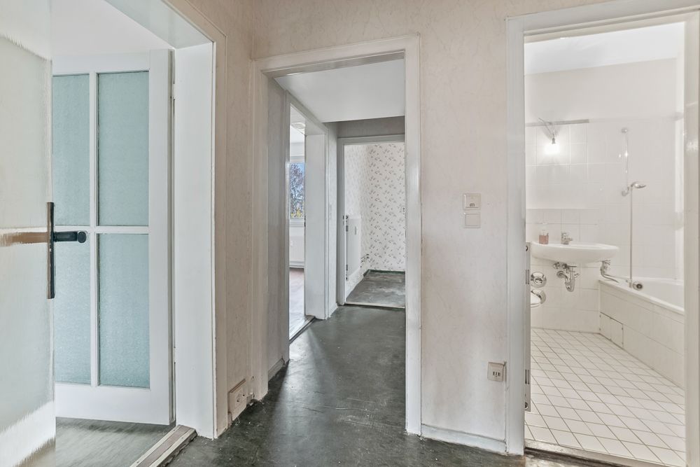 Flur mit drei Türen, eine davon führt in ein Badezimmer mit weißen Fliesen und Badewanne.