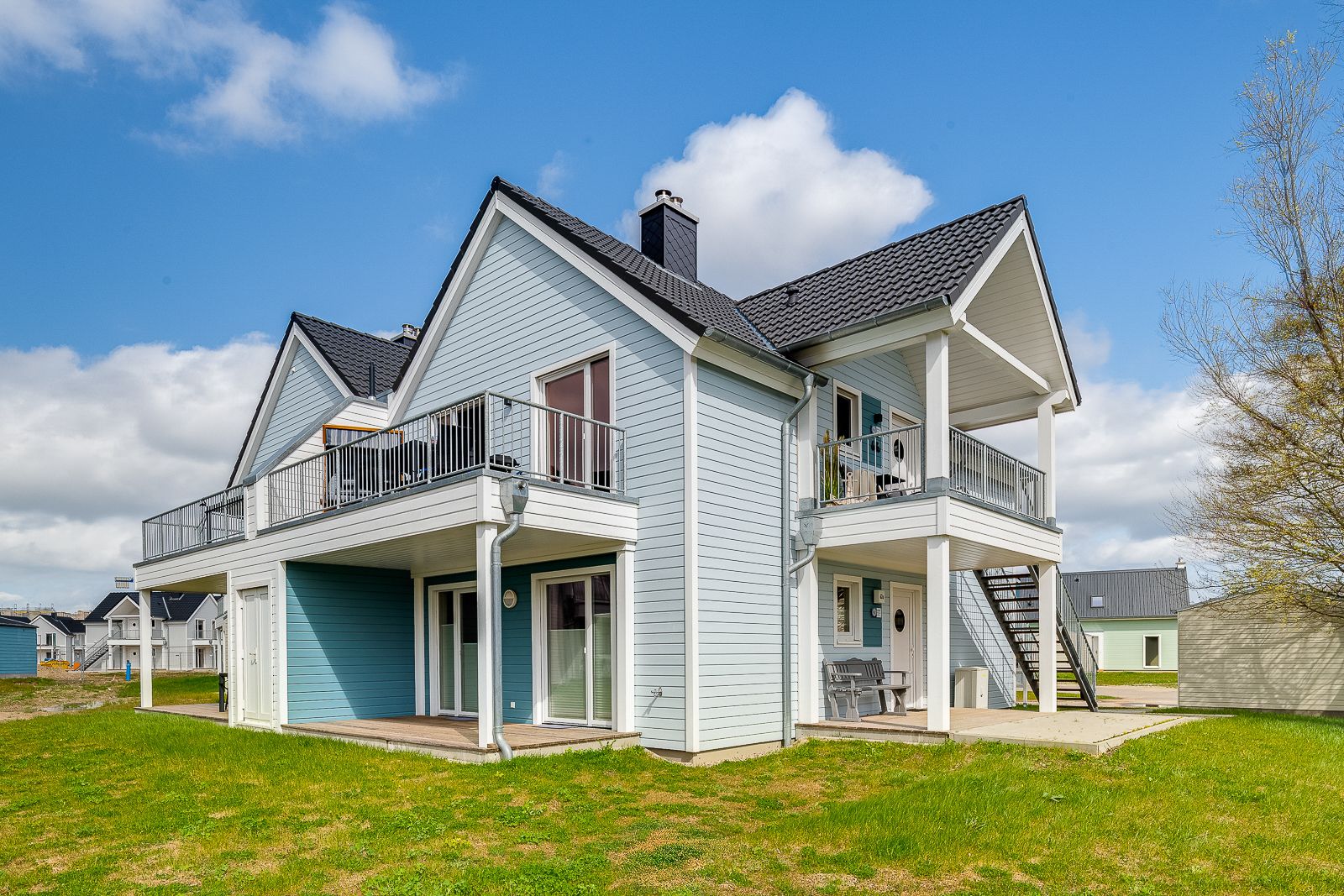 Modernes zweistöckiges Haus mit hellblauer Fassade, Balkon und Außentreppe im Garten.