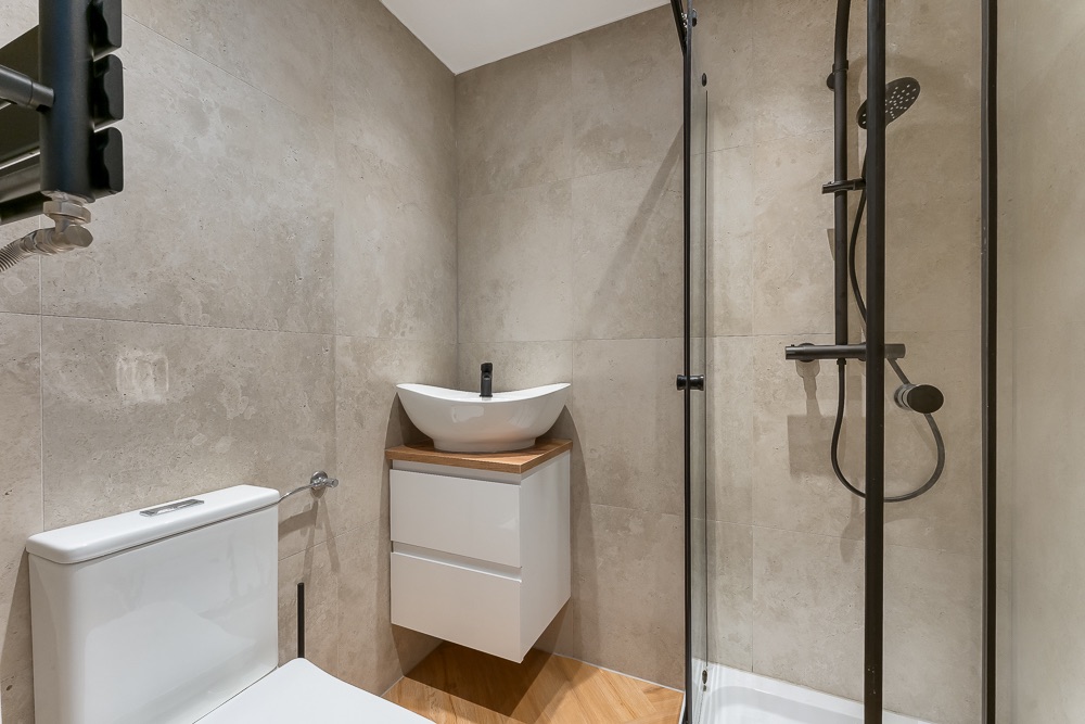 Modernes Bad mit Toilette, Waschbecken und Glasdusche auf beigem Fliesenboden.