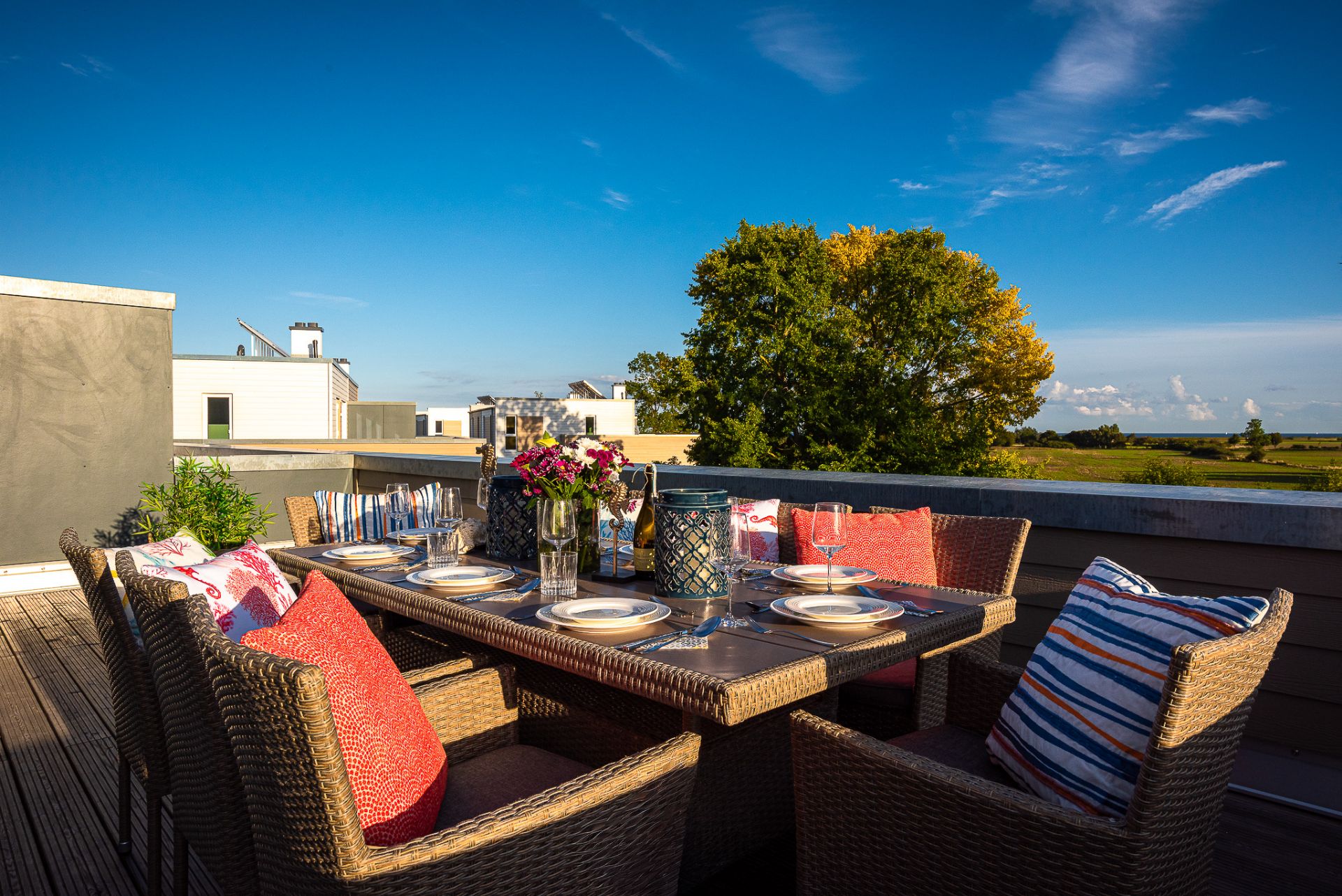 Gedeckter Esstisch mit Stühlen und Kissen auf einer Terrasse mit Aussicht auf Bäume und Wiese.