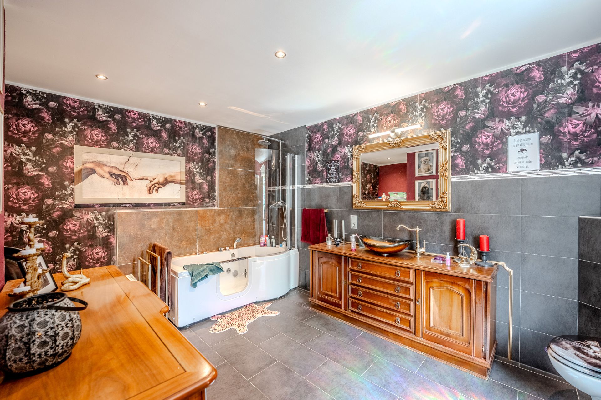Großes Bad mit Badewanne, Spiegel, Holzkommode und floraler Tapete.
